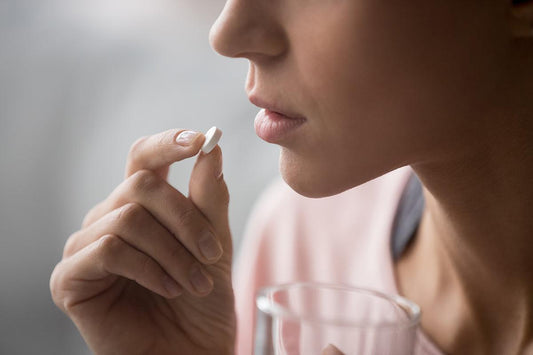 A close-up of a woman with a glass of water. She's holding an OTC pain reliever to her lips.