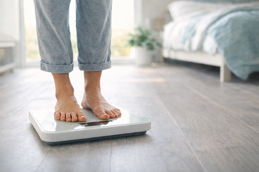 The legs and feet of a woman in a bedroom, standing on a scale