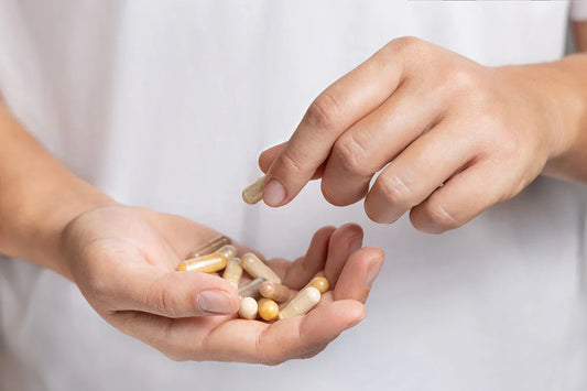 Close-up photo of a woman's hands. One hand is cupping a handful of supplements, the other hand holds one capsule