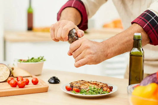 A man's arms are seen adding seasoning to a plate of grilled meat