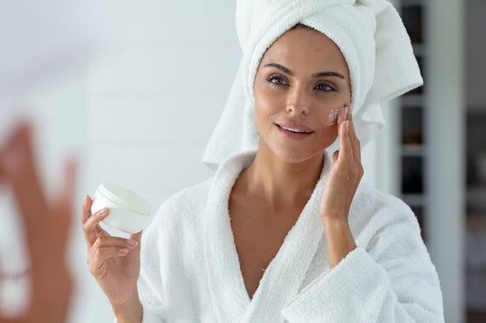 A beautiful woman wearing a robe applies skin care to her face