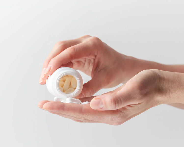 A pair of  hands pouring capsules out of a white supplement bottle