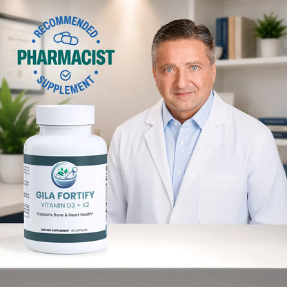 A white bottle of Gila Fortify Vitamin D3 + K2 dietary supplement is shown in the foreground on a white table, with a male pharmacist in a white lab coat standing behind it in a bright office setting. A blue circular badge on the top left reads 'RECOMMENDED PHARMACIST SUPPLEMENT'.