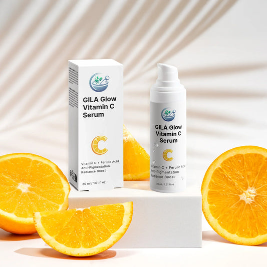 GILA Glow Vitamin C Serum bottle and its white box, positioned on white display blocks, surrounded by bright orange slices. A soft, blurred palm frond is visible in the background.
