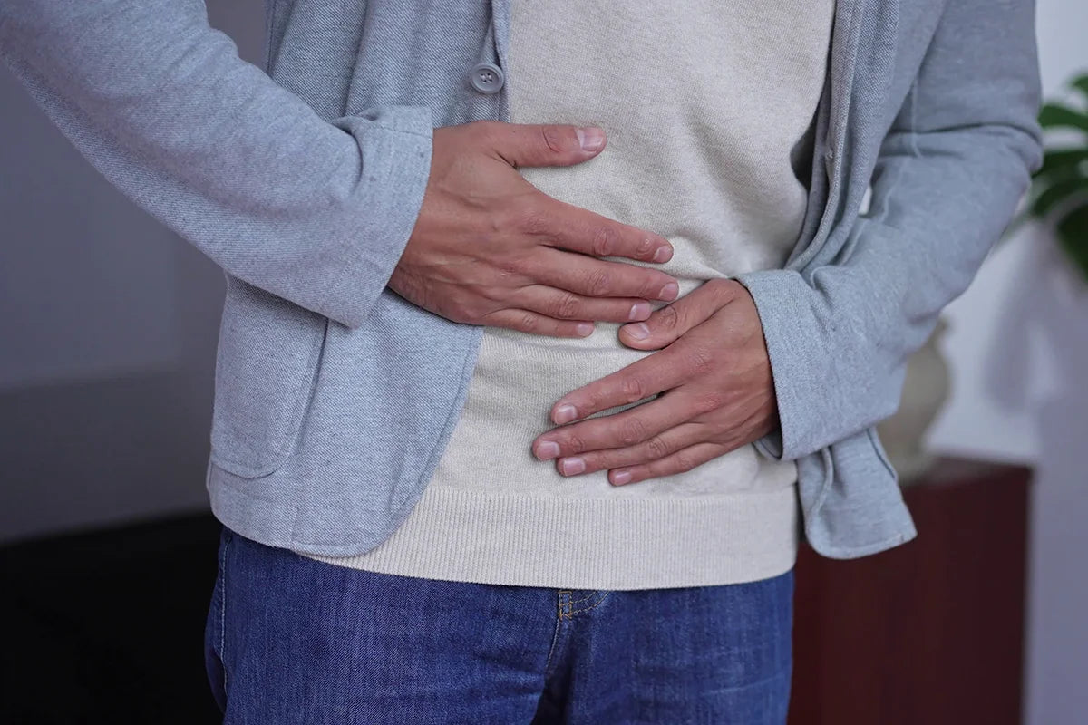 A man wearing blue jeans and a sweater clutches his stomach