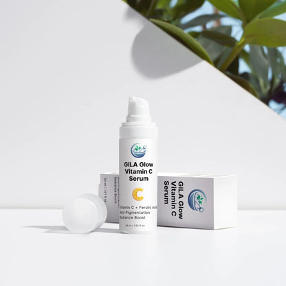 An image of the GILA Glow Vitamin C Serum with lid off, and the box on its side. It's on a white outdoor background, with shrubs peeking up from behind