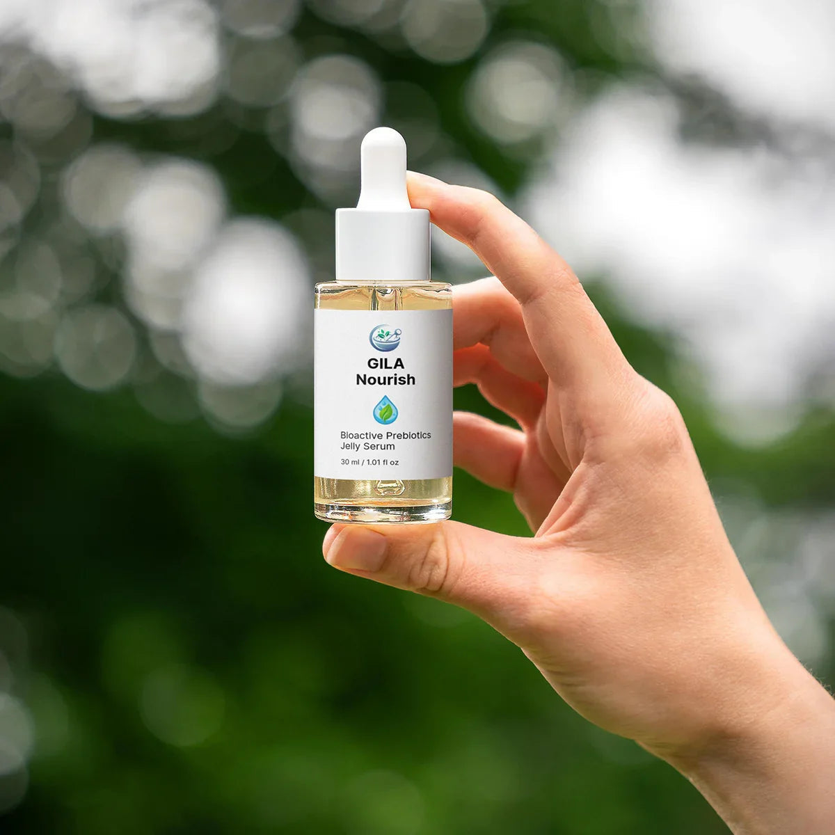 Hand holding a bottle of Gila Nourish serum against a blurred green background