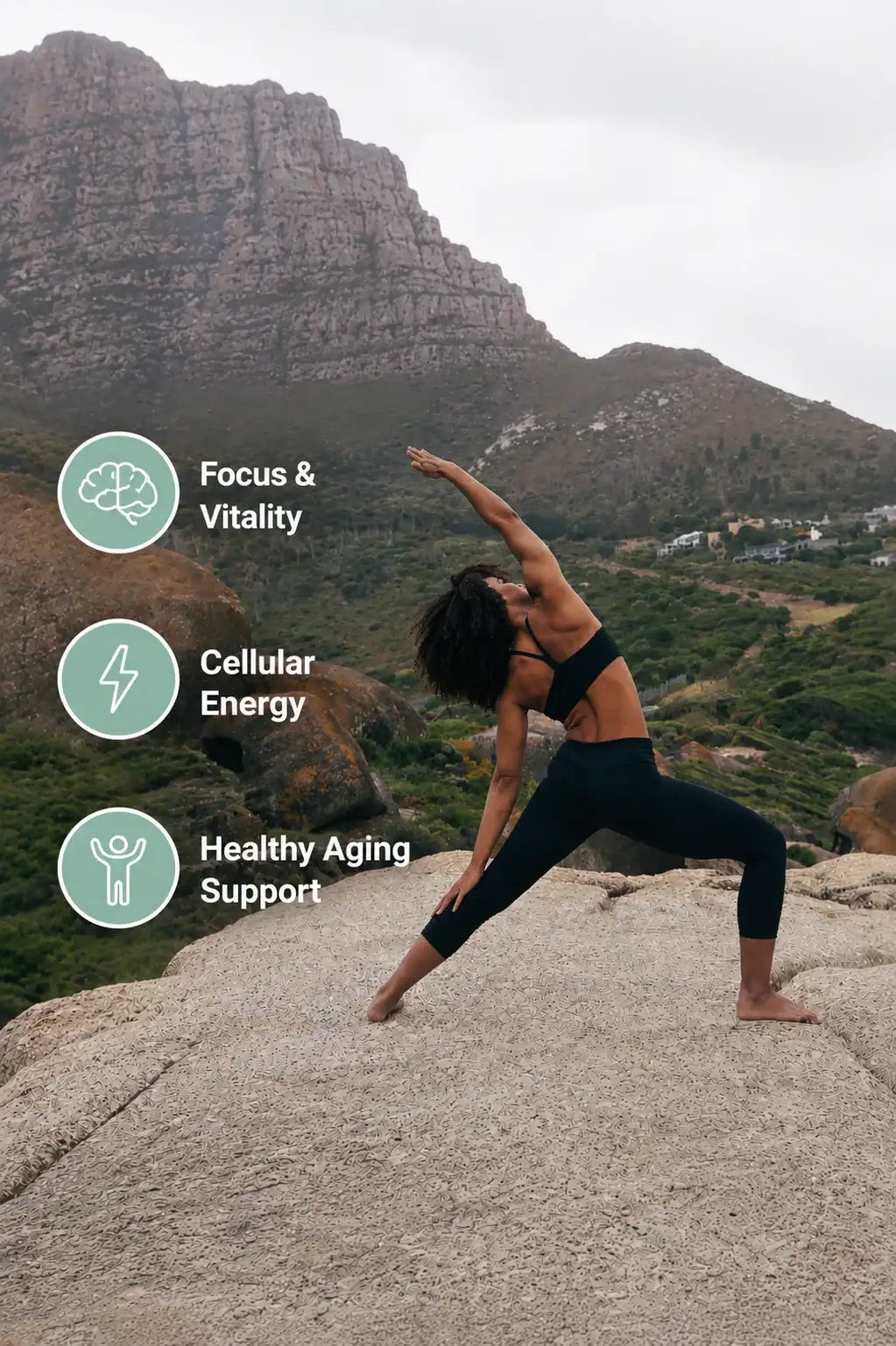 A woman in black athletic wear performs a yoga pose on a rocky outcrop.